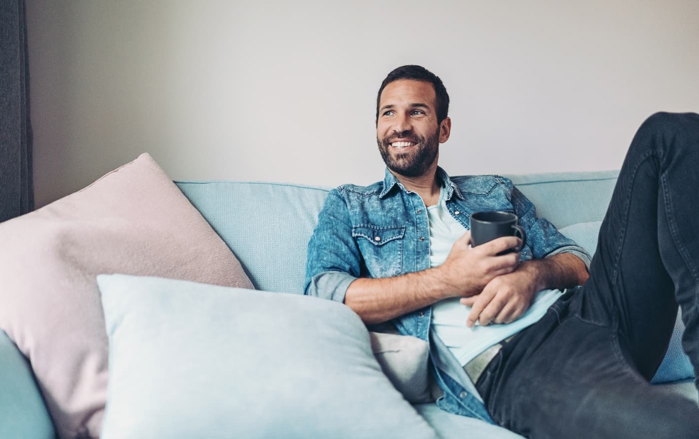 Man relaxing comfortably on a couch with a cup of coffee β the calm and safety that trauma therapy at MMHC helps restore